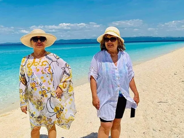 Zwei Frauen stehen an einem weißen Sandstrand auf Kalanggaman Island mit klarem blauem Wasser