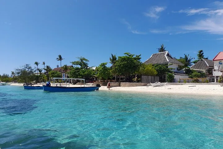 Klares blaues Wasser mit einem Boot und Küstengebäuden mit Palmen