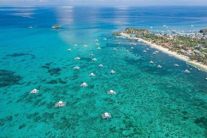 Luftaufnahme einer Küstenstadt mit vielen Auslegerbooten, die in klarem Wasser vor Anker liegen.