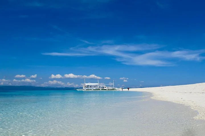 Ein weißes Auslegerboot, das nahe einer weißen Sandbank vor Anker liegt, die in klares blaues Wasser reicht.