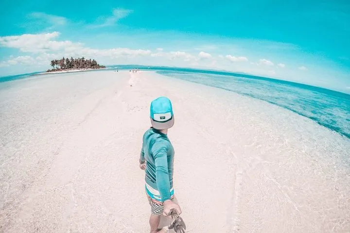 Personne tenant une perche à selfie marchant sur un banc de sable blanc de l’île de Kalanggaman