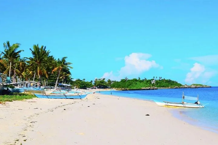 Spiaggia di sabbia bianca fiancheggiata da palme e barche sull'isola di Kalanggaman